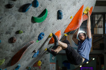 Young Active Sport Caucasian American Bearded Man In Glasses And T-shirt Climbing On Wall With Color Holds During Bouldering Training Session