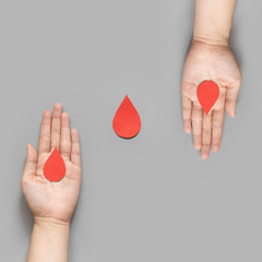 Wall Mural - Blood donation - Human hand giving blood drop symbol to a hand on gray background. World blood donor day and save life concept. Flat lay.