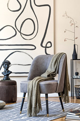 Wall Mural - Stylish beige interior of living room with design gray armchair, brown pouf, plaid, black shelf and elegant personal accessories. Abstract paintings on the wall. Modern home staging. Template.