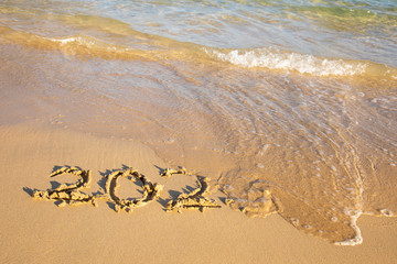 2020 summer beach holiday season written on golden sand washed away wave - new season lettering on sand - numbers 2020 year travel vacation sandy wavy water yellow blue azure aquamarine turquoise