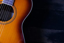 Cropped Image Of Vintage Style Travel Size Acoustic Guitar With Rosewood Neck And No Pickguard On Grunged Dark Wood Textured Background. Close Up, Copy Space For Text, Top View.