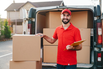 Wall Mural - Image of smiling delivery man writing while standing with parcel boxes