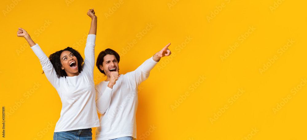Multiracial couple dancing and singing together, having fun over yellow background - obrazy, fototapety, plakaty 
