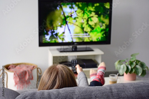 Fotomural Young woman watching television with subtitles while sitting comfortably on sofa at home in living room