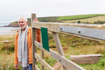 Wall Mural - Active Senior Man Walking Along Coastal Path In Winter Opening Gate With Beach And Cliffs Behind