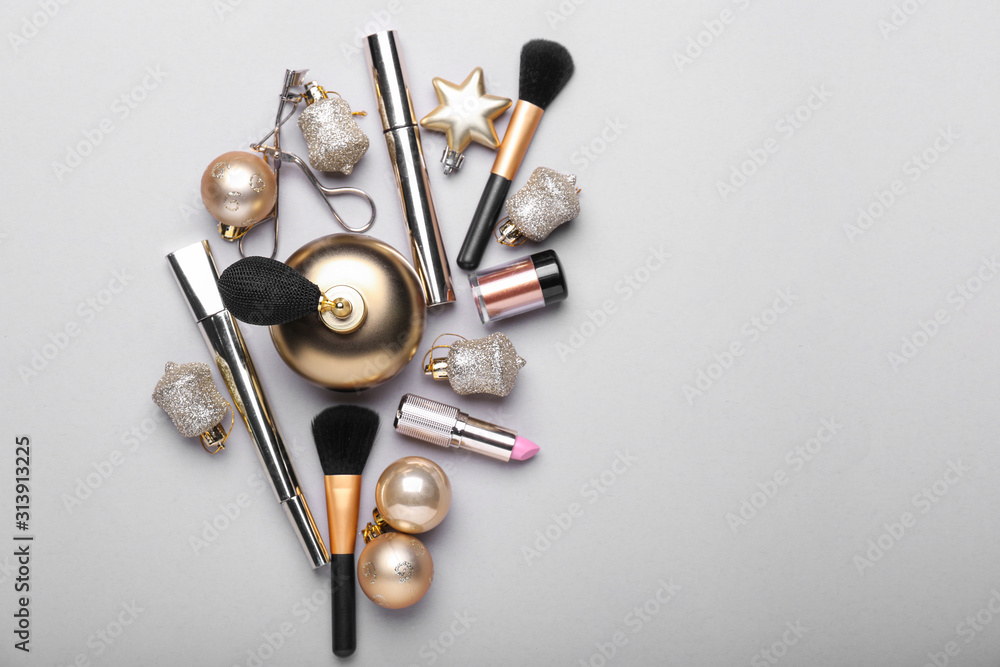 Bottle of perfume with makeup cosmetics and Christmas decor on grey background