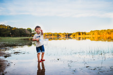 Excited Young Boy Holding Small Fish He Caught At The Lake