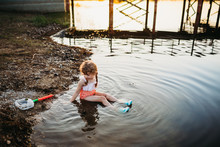 Young Girl Sitting In Water At Lake And Catching Fish With Net