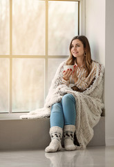 Sticker - Young woman drinking hot tea on window sill at home