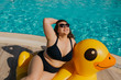 © Julia - Curvy woman resting by the pool with yellow inflatable duck.