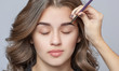 © Dimid - Make-up artist does eyebrow make-up to a woman with curly brown hair and nude make-up. Beautiful thick eyebrows close up. Professional makeup and cosmetology skin care.