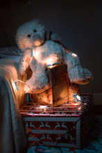 Teddy Bear Sitting On Gifts Under The Tree. Christmas Gifts, Garlands And Toys.