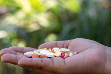 Many medicines in the hands of people on a blurred green nature background.