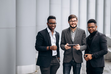 Poster - Businesspeople of different nationalities. Three attractive business men stand near the business center in suits outdoors.