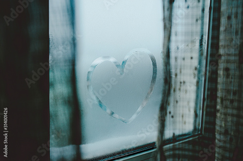 beautiful smooth heart is drawn with a finger on wet sweaty glass, drops flow down the window with curtains on the sides
