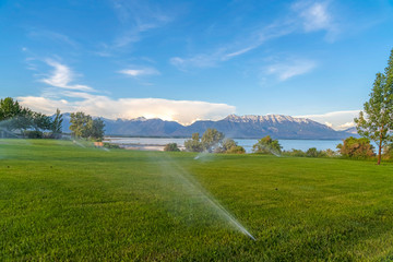 Wall Mural - Lake and snow capped mountain with sprinklers on green grasses in foreground