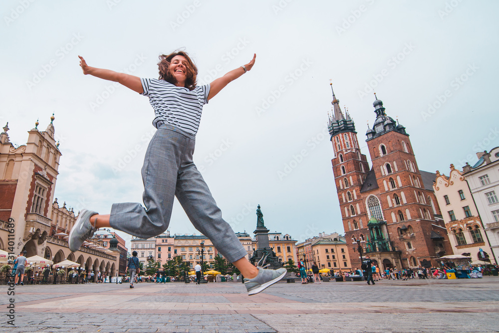 Obraz city tourism concept woman jumping at krakow market square saint mary church on background fototapeta, plakat