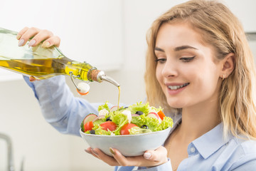 Young woman pouring olive oil in to the salad. Healthy lifestyle eating concept