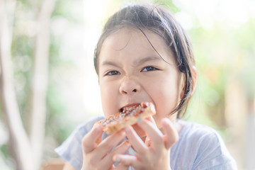 Wall Mural - Funny little asian girl eating tasty toasts with strawberry jam spread for breakfast. Hungry face and Delicious face in kid girl.