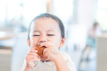 Wall Mural - Cute little asian toddler boy holding soft bread at home.Hungry toddler boy make delicious face when he eating bakery.