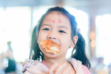 Wall Mural - Cute little asian girl holding and eating soft bread at home.Hungry kid girl make delicious face when she eating bakery.