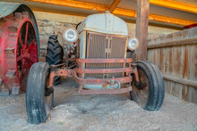 Front Of An Old And Vintage Tractor Against Stone Wall And Roof Of A Farm Barn