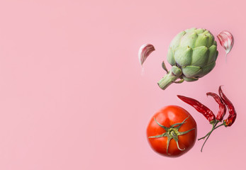 Organic vegetables artichoke ripe juicy tomato hot chili peppers garlic cloves floating levitating on pink background. Creative food poster. Mediterranean cuisine healthy diet ingredients