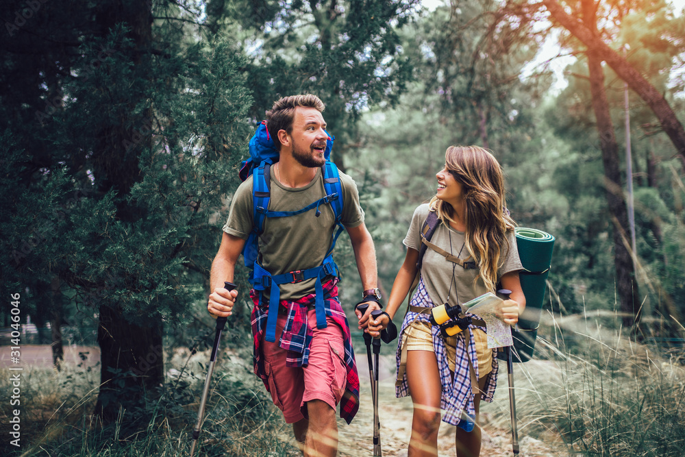 Smiling couple walking with backpacks over natural background - obrazy, fototapety, plakaty 