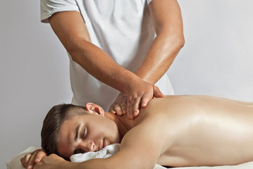 Massage therapist in a white T-shirt doing a back massage. The guy lies on the table on a white background. Manual therapy.