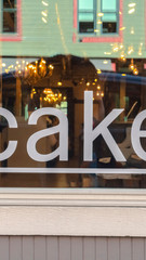 Vertical Close up of a white cake sign on the shiny glass window of a store building