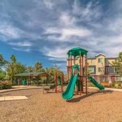 Wall Mural - Square frame Park with playground and pavilion against townhouses and blue sky with clouds