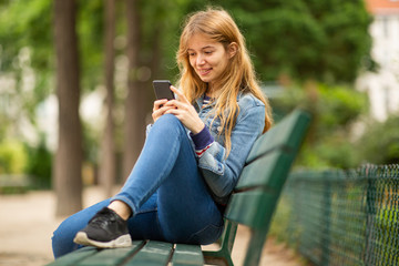 young woman sitting on park bench looking at phone