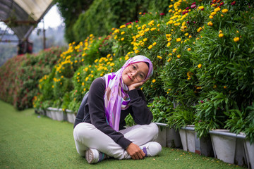 Wall Mural - Beautiful attractive muslim young woman sitting with colorful flowers park background at Cameron Highlands