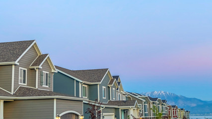 Wall Mural - Pano frame Exterior of homes with gable and valley roofs against mountain and sky at sunset