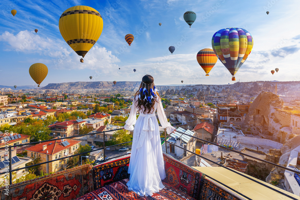 Beautiful girl standing on the hotel and looking to hot air balloons in Cappadocia, Turkey. - obrazy, fototapety, plakaty 