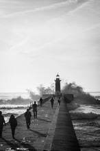 Black And White Photo, Waves Break Down To The Pier Under The Lighthouse.  Sunset Lighthouse. Lighthouse As A Ladmark. Foz Do Douro. Porto. Portugal