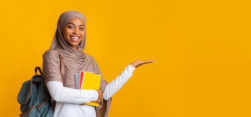 Wall Mural - Cheerful black islamic female student in hijab pointing aside with hand