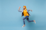 Fototapeta  - Cheerful young hipster guy in fashion jeans denim clothes posing isolated on pastel blue background studio portrait. People sincere emotions lifestyle concept. Mock up copy space. Jumping, running.