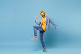 Fototapeta  - Laughing young hipster guy in fashion jeans denim clothes posing isolated on pastel blue wall background studio portrait. People emotions lifestyle concept. Mock up copy space. Doing winner gesture.