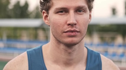 Wall Mural - Close up view of smiling curly handsome man looking at the camera and talking something on stadium outdoors