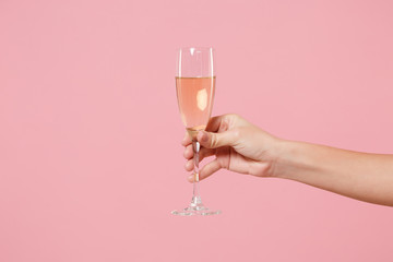 Close up cropped photo of female hold in hand glass of champagne isolated on pastel pink wall background. Copy space advertising mock up. Valentine's Day Women's Day birthday holiday party concept.