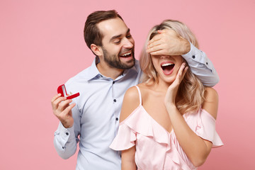 Cheerful couple two guy girl in party outfit celebrating isolated on pink background. Valentine's Day Women's Day birthday holiday concept. Hold present box with proposal ring covering eyes with hand.