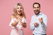 © ViDi Studio - Cheerful young couple two guy girl in party outfit celebrating posing isolated on pastel pink wall background. Valentine's Day Women's Day birthday holiday concept. Pointing index fingers on camera.