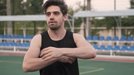 Wall Mural - Focused handsome man stretching with hands and looking away on stadium outdoors