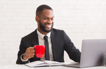Smiling black man in suit drinking coffee in office