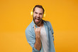 Crazy young man in blue shirt posing isolated on yellow orange background. People lifestyle concept. Mock up copy space. Listen music with headphones, showing horns up gesture, heavy metal rock sign.