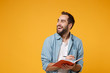 © ViDi Studio - Cheerful young student man in casual blue shirt posing isolated on yellow orange wall background, studio portrait. People lifestyle concept. Mock up copy space. Writing note in notebook looking aside.