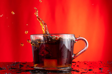 brewing tea from a tea bag in a large wide transparent mug, a splash of sugar falling