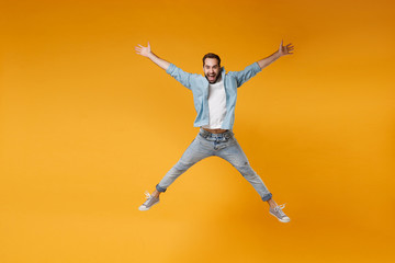 Sticker - Joyful young bearded man in casual blue shirt posing isolated on yellow orange wall background studio portrait. People emotions lifestyle concept. Mock up copy space. Jumping, spreading hands, legs.