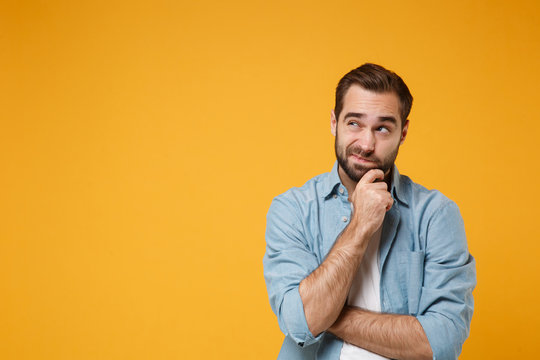 pensive young bearded man in casual blue shirt posing isolated on yellow orange background studio po